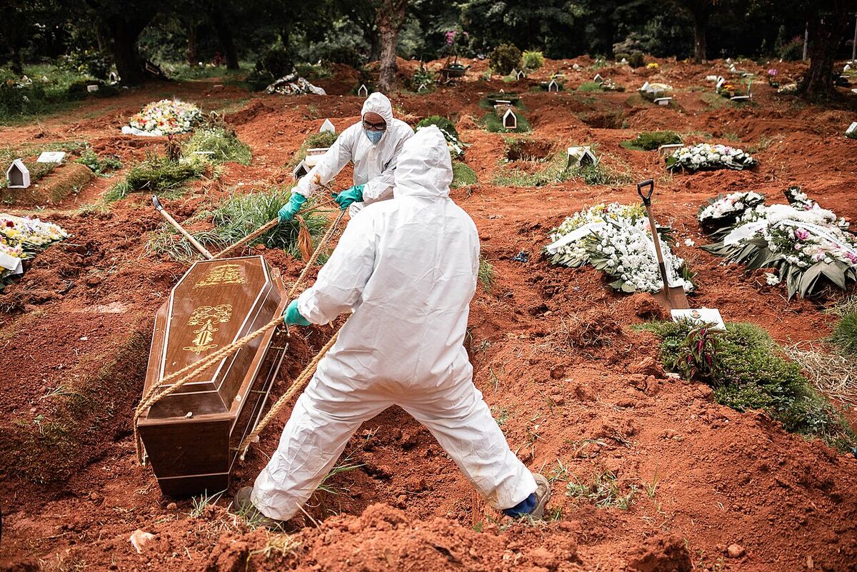 Sepultadores com equipamento de proteção enterram uma vítima da covid-19 em São Paulo, em abril de 2020
